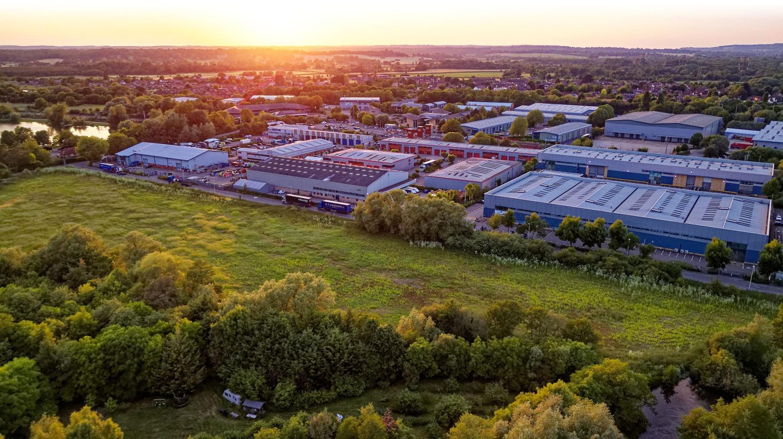Aerial view of a UK industrial park at sunrise, warehouse units set among trees and open ground