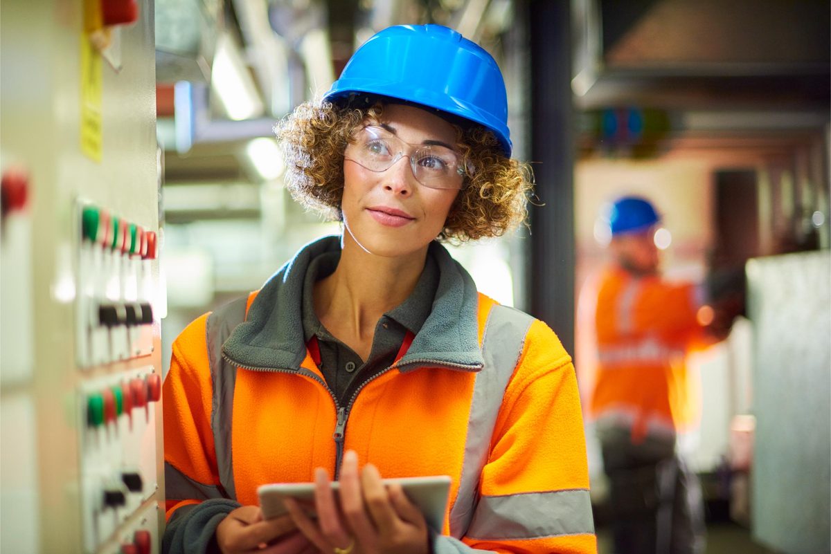 An engineer in hi-vis and a hard hat checking equipment on a tablet in a plant room